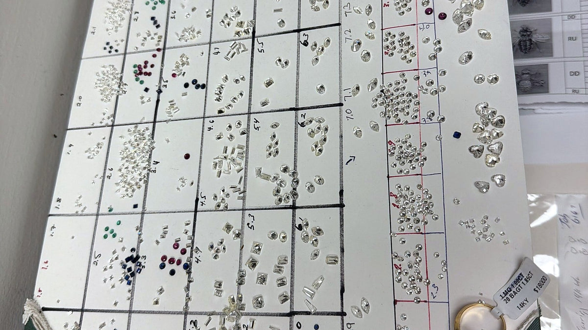 A jeweler's stone board on the desk at Benji Designs, loose diamonds and colored stones sorted into numbered squares.