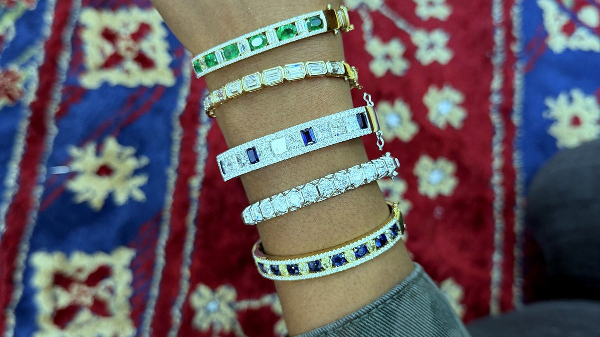 Five diamond and gemstone bangles worn stacked on a wrist, a sweatshirt cuff at the edge of the frame.