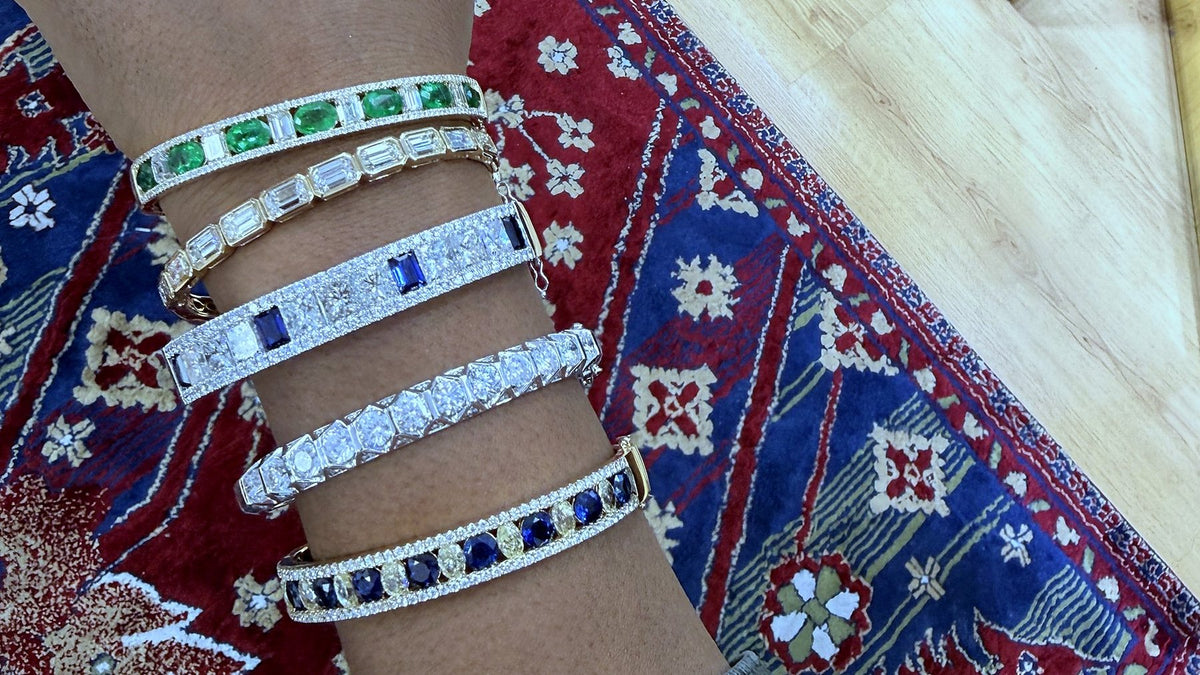 Five diamond and gemstone bangles worn stacked on a wrist.